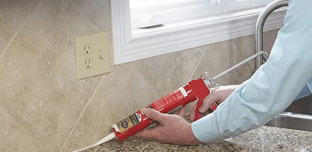 Handyman applying caulk along a kitchen backsplash and countertop seam in Mesa, AZ